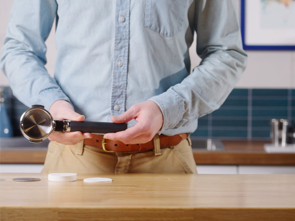 Talent holding the Weber Workshops Buck Portaiflter with an array of paper filters spread on a counter lifestyle by Clive Coffee